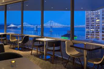 A room with tables and chairs and a bridge in the background Description automatically generated